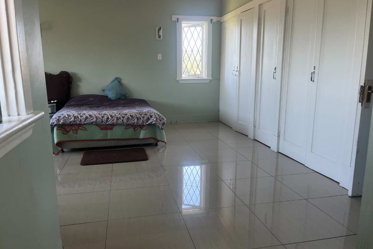 Spacious bedroom featuring large format floor tiles, built-in cabinetry, and a leaded glass window, offering a clean and functional living space.