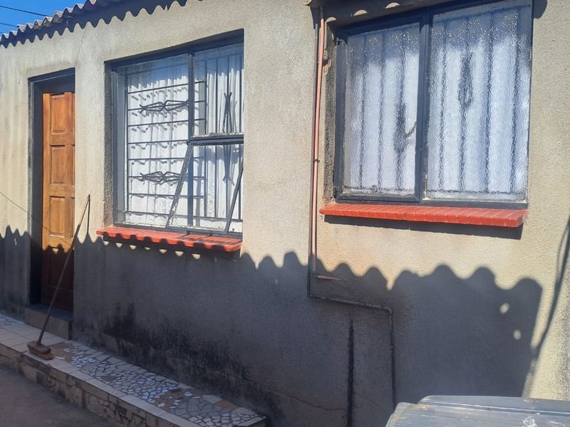 Exterior view of the property showing plastered walls, security bars on windows, and tiled window sills.