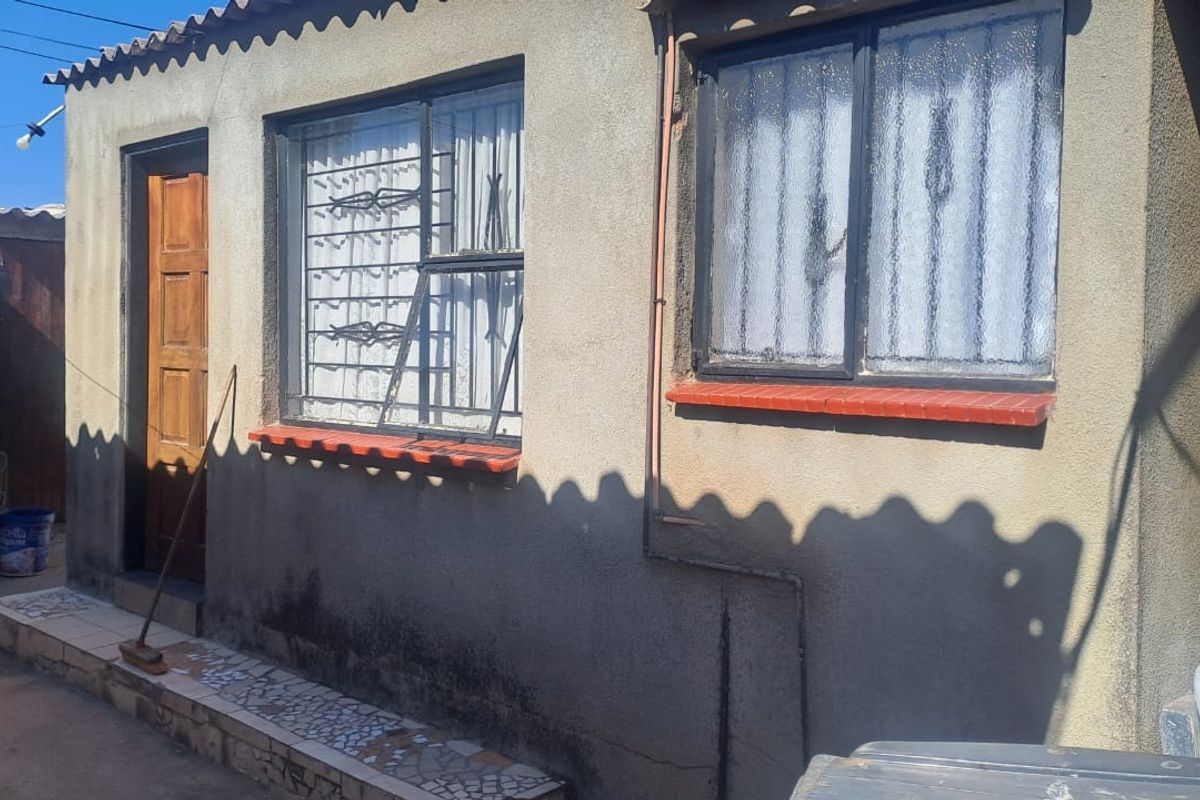 Exterior view of the property showing plastered walls, security bars on windows, and tiled window sills.