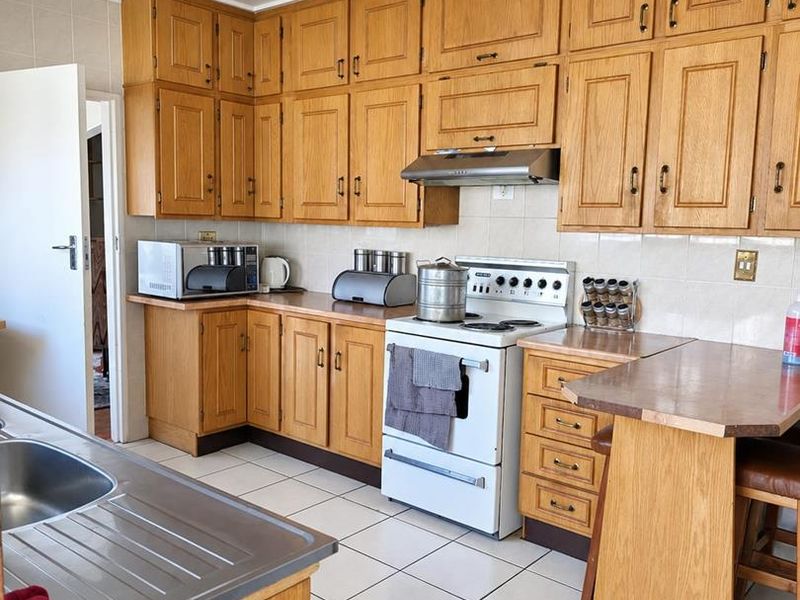 A functional kitchen featuring traditional wooden cabinetry, tiled flooring, a breakfast counter, and a built-in extractor fan over the stove area.