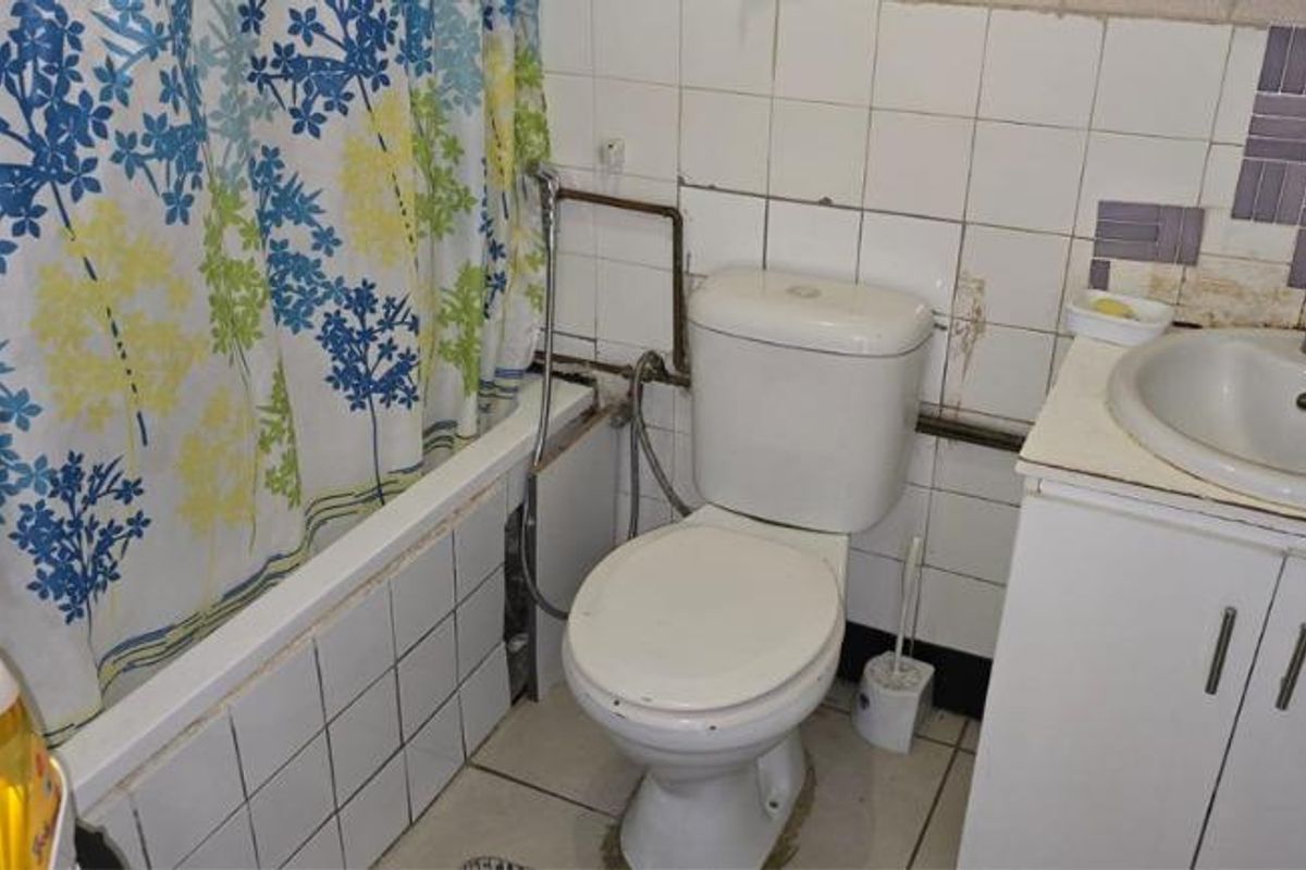 A dated bathroom featuring a bathtub, toilet, and vanity basin with tiled finishes, currently requiring significant maintenance and cosmetic updates.