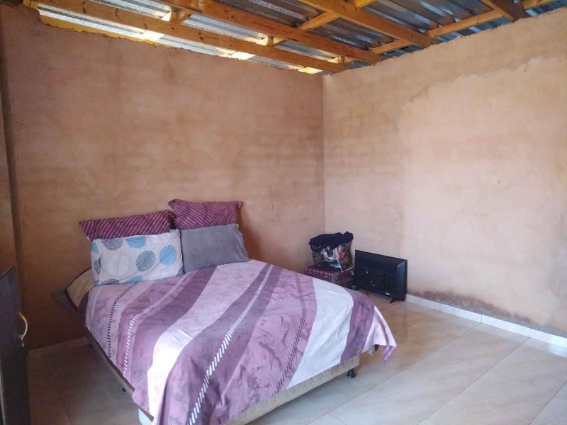 A bedroom featuring tiled flooring and exposed timber roof rafters, currently requiring ceiling installation and wall finishing to improve the overall condition.