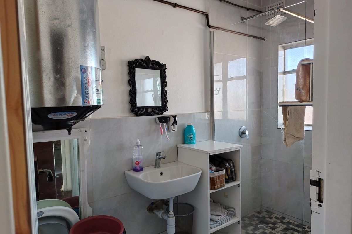 A functional bathroom featuring a wall-mounted water heater, ceramic basin, and a glass-enclosed shower with exposed copper piping.