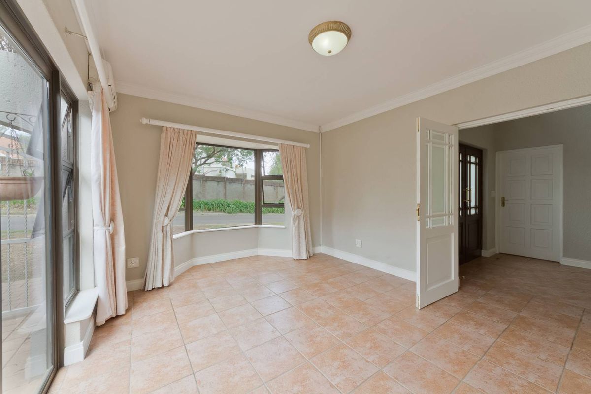 A bright, empty living room featuring tiled flooring, a large bay window, and direct access to an outdoor area via a sliding glass door.