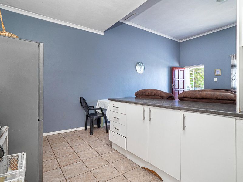 A functional kitchen area featuring built-in white cabinetry, dark laminate countertops, and tiled flooring, with direct access to the living space.