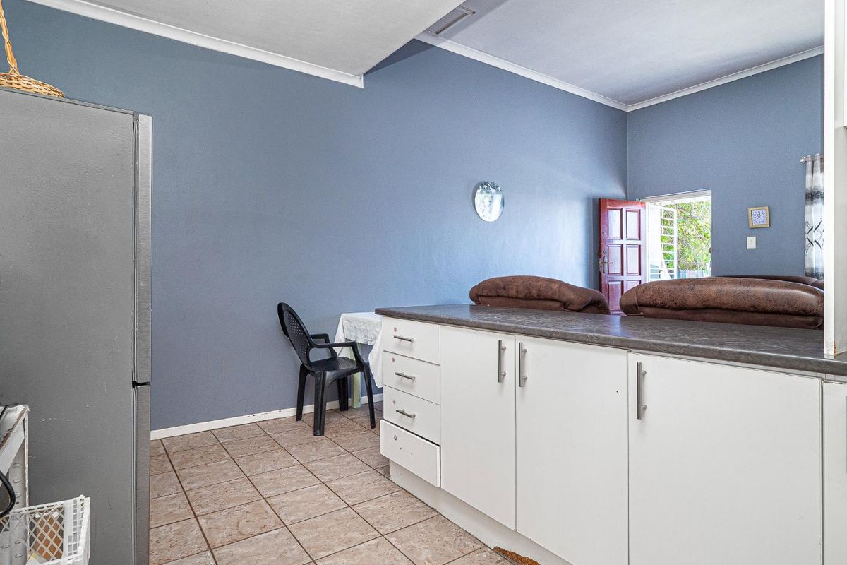 A functional kitchen area featuring built-in white cabinetry, dark laminate countertops, and tiled flooring, with direct access to the living space.