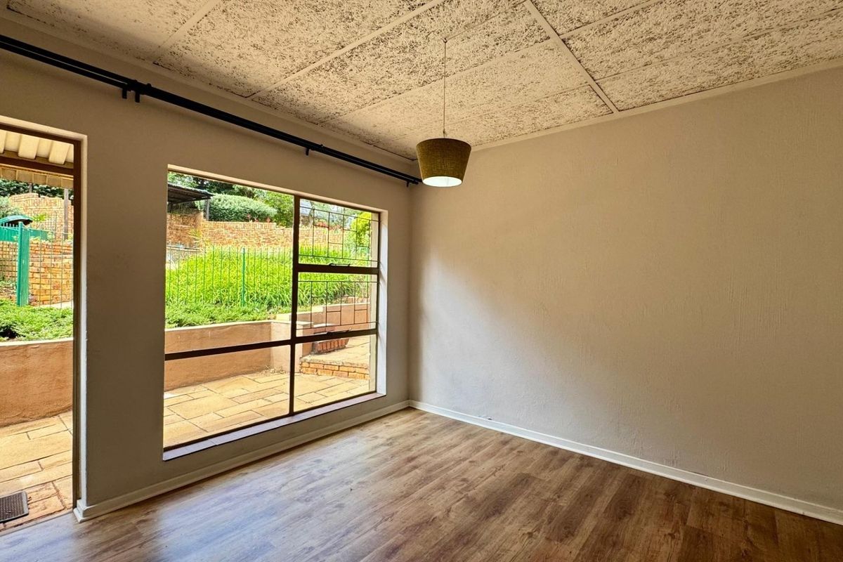 An empty living room featuring laminate flooring, textured ceiling tiles, and a large window providing natural light and access to the outdoor patio area.