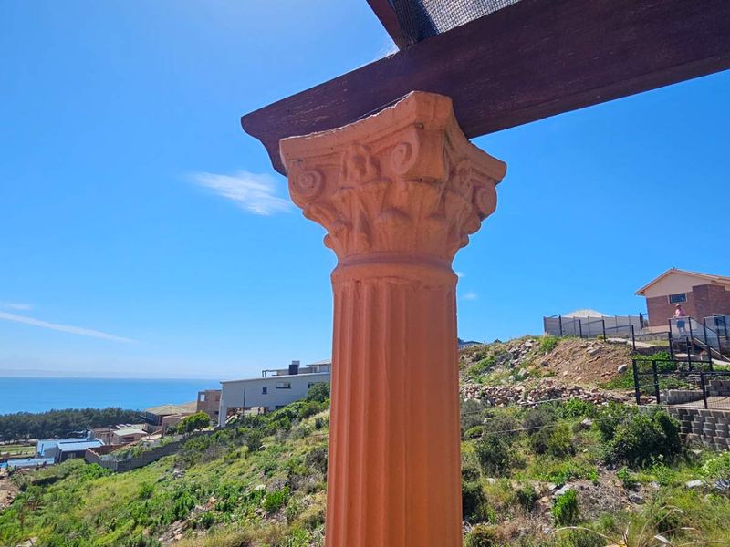 A view from a patio featuring a decorative column and pergola, overlooking the surrounding landscape and ocean.
