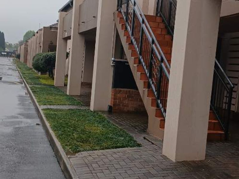 Exterior view of an apartment complex featuring paved walkways, landscaped grass patches, and external staircases with metal railings leading to upper-level units.