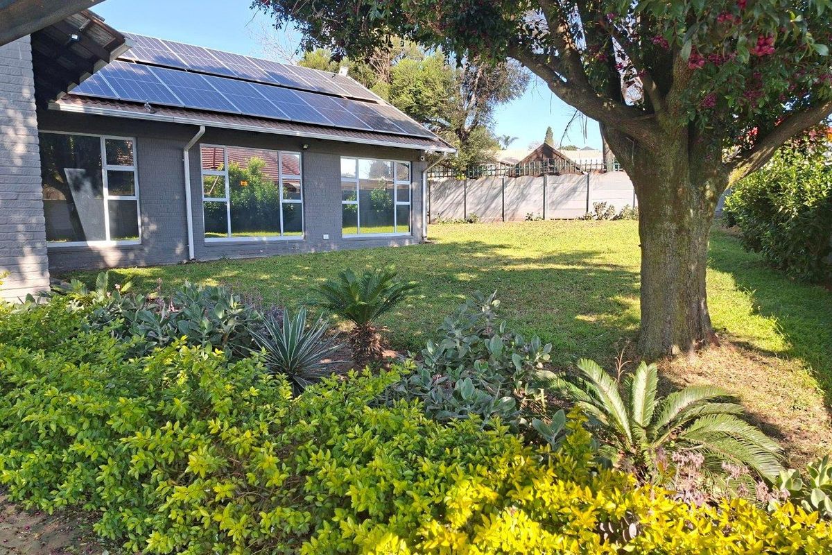 Rear view of the property featuring a well-maintained garden, established trees, and a roof-mounted solar panel system.