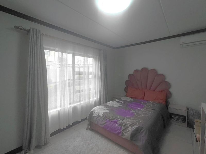A bedroom featuring tiled flooring, an installed air conditioning unit, and large windows with curtain rails.