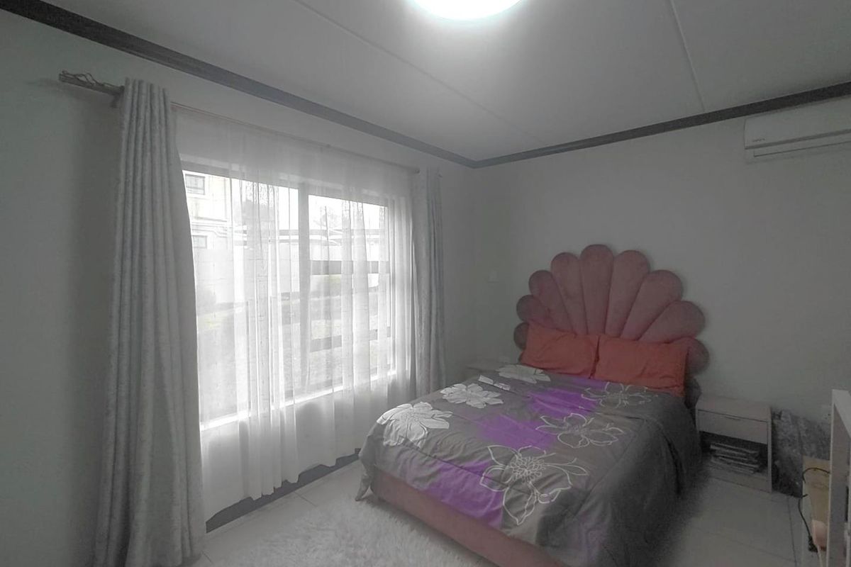 A bedroom featuring tiled flooring, an installed air conditioning unit, and large windows with curtain rails.