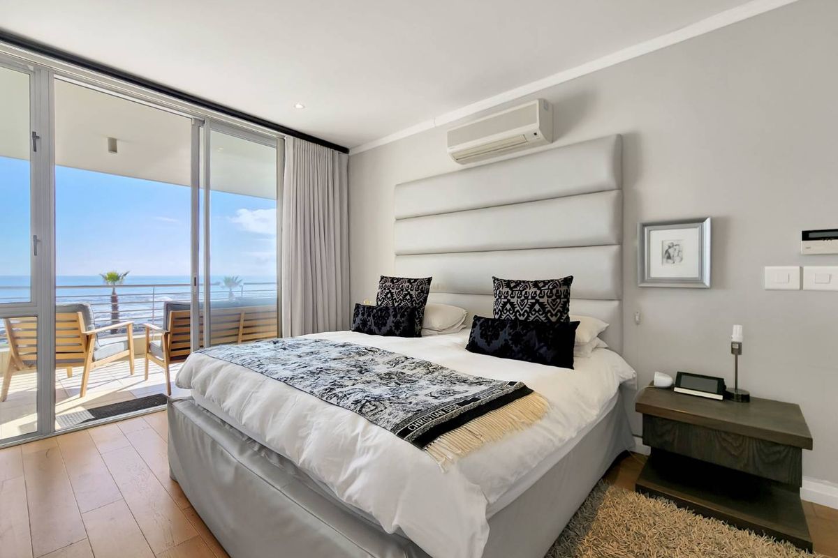A well-maintained bedroom featuring hardwood flooring, an integrated air conditioning unit, and large sliding glass doors opening onto a balcony with ocean views.