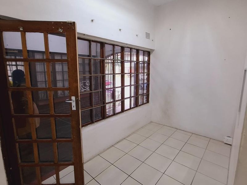 A vacant office space featuring tiled flooring, timber-framed windows with security bars, and a matching timber-framed glass door.