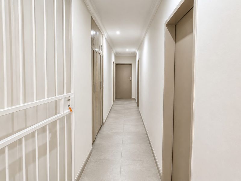 A clean, well-lit hallway featuring neutral tiled flooring, built-in storage cabinetry, and a secure metal gate at the entrance.