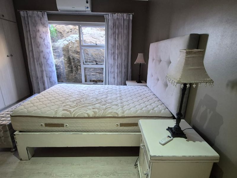 A well-lit bedroom featuring built-in cupboards, laminate flooring, and a split-system air conditioner, with a view of a natural rock formation outside.