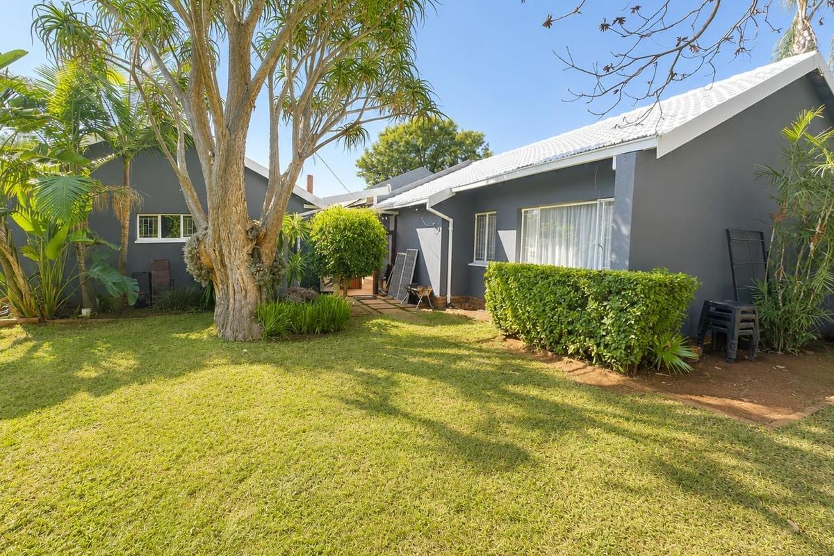 A well-maintained rear exterior view of the house featuring a spacious lawn, mature trees, and a paved pathway leading to the building entrance.