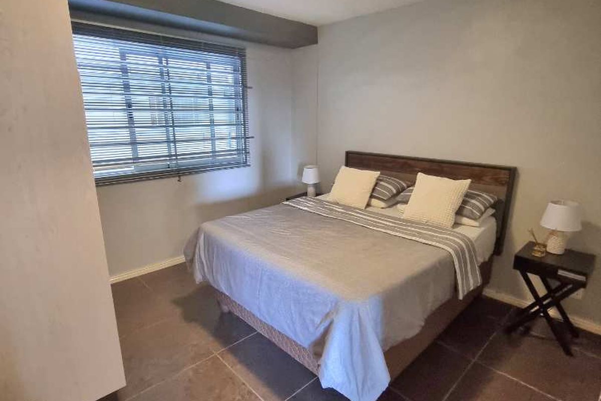 A functional bedroom featuring tiled flooring, a built-in wardrobe, and a window with fitted blinds, providing a neutral space for rest.