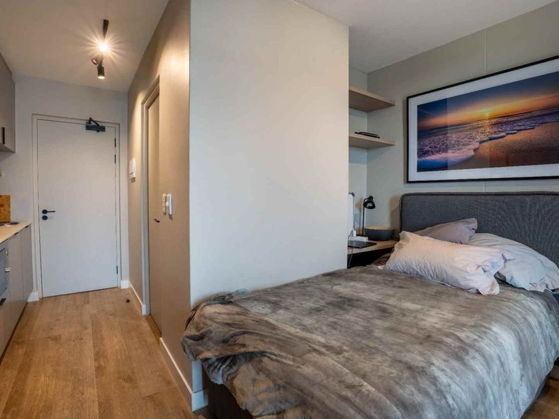 A compact open-plan studio apartment featuring modern cabinetry, laminate flooring, and efficient use of space with integrated shelving and lighting.