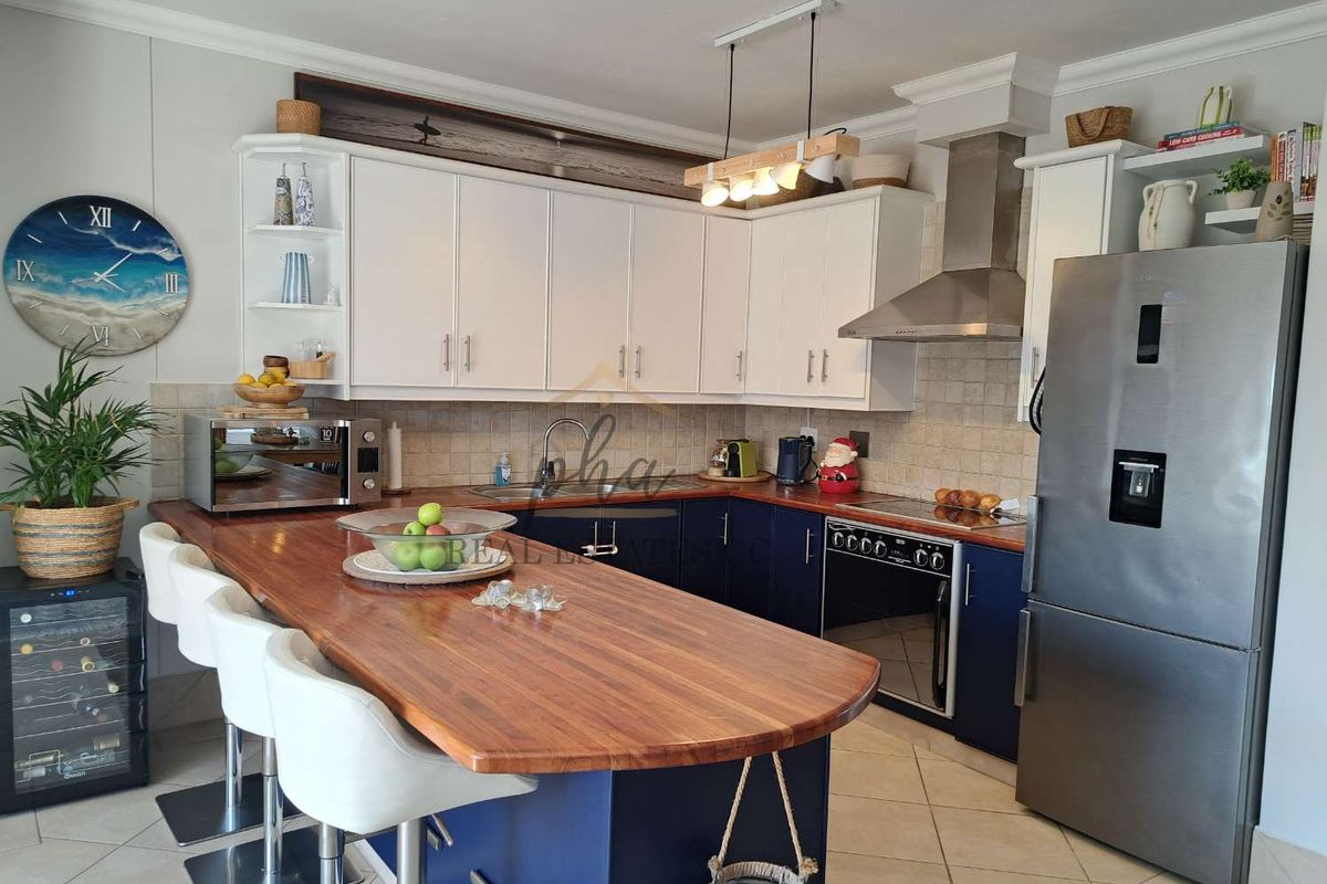 Modern kitchen featuring blue lower cabinetry, white upper cabinets, wooden breakfast bar, stainless steel extractor fan, and tiled backsplash.