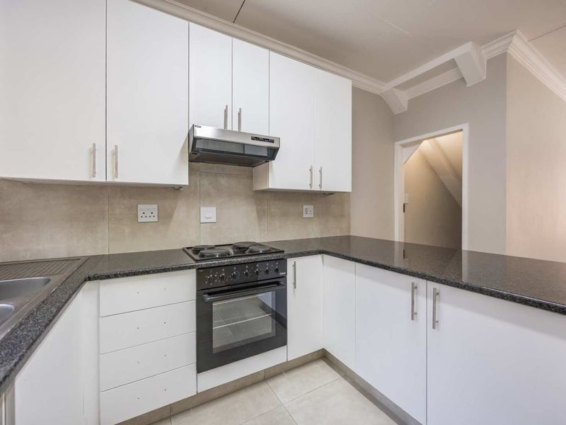 A clean, modern kitchen featuring white cabinetry, dark granite countertops, a built-in oven with gas hob, and neutral tiled flooring.