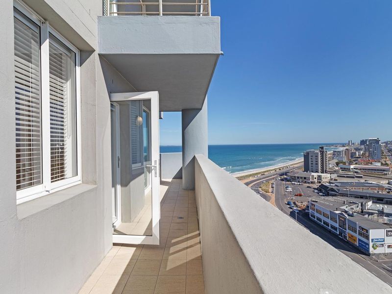 A spacious balcony featuring tiled flooring and a glass door, offering expansive coastal and urban views.