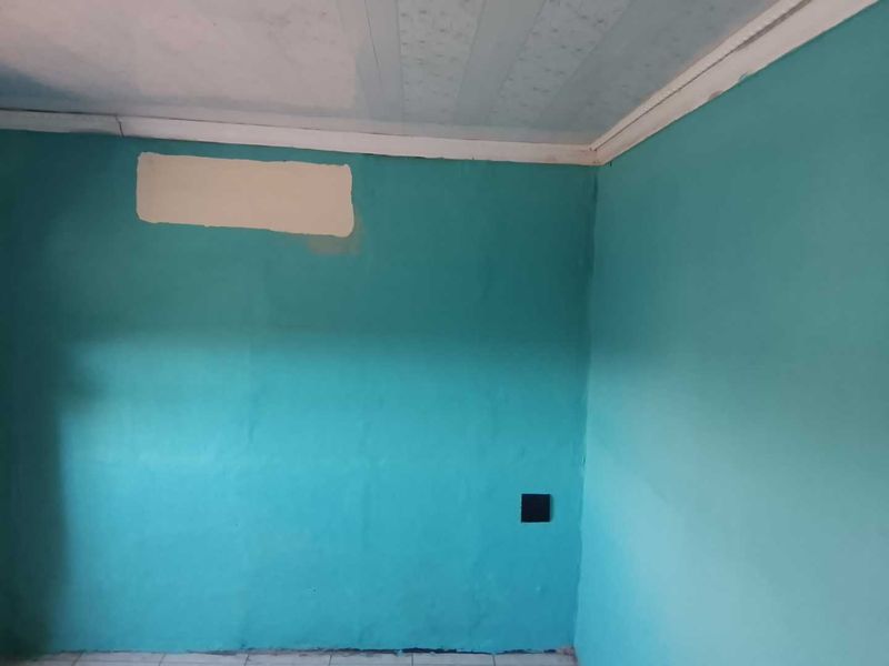 An empty room featuring teal painted walls with visible surface imperfections and a textured ceiling, requiring cosmetic updates to improve its overall condition.