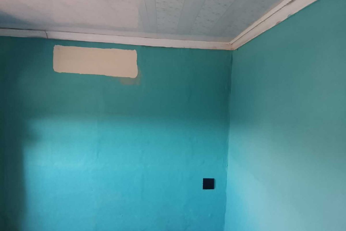 An empty room featuring teal painted walls with visible surface imperfections and a textured ceiling, requiring cosmetic updates to improve its overall condition.