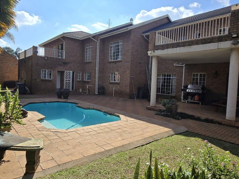 Rear exterior view featuring a swimming pool, paved patio area, and a multi-level brick house with a covered entertainment space.