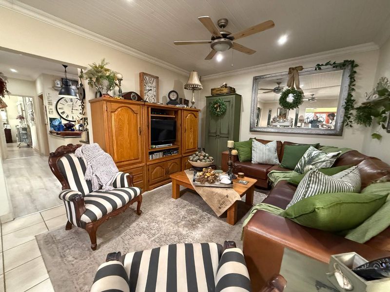 A cozy living room featuring a plank ceiling, crown molding, and a ceiling fan, with an open transition to the adjacent hallway area.