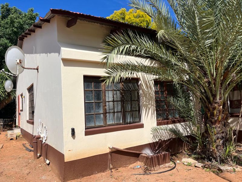 Rear exterior view of the house featuring a corrugated metal roof, timber-framed windows, and external plumbing fixtures set against a garden area.
