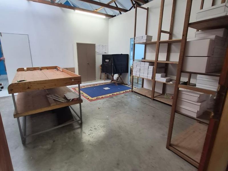 Spacious office area featuring exposed timber roof trusses, concrete flooring, and built-in shelving, offering a functional workspace with industrial character.