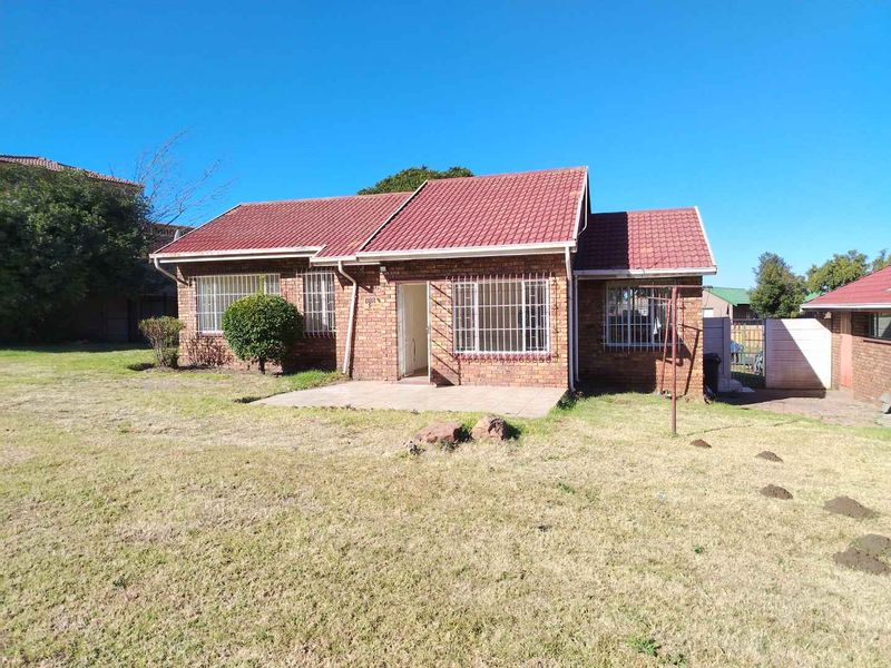 A single-story facebrick house featuring a tiled roof, security bars on windows, and a paved front patio area set within a spacious garden.