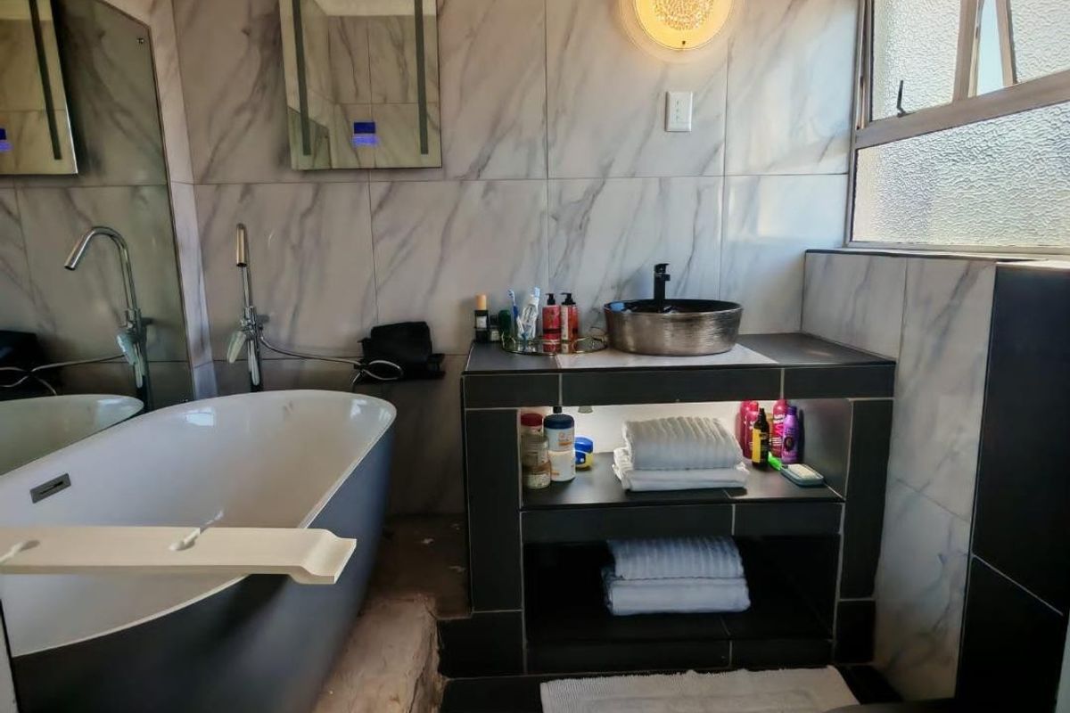Modern bathroom featuring a freestanding bathtub, vessel sink, built-in vanity shelving, and marble-look wall tiles with a functional casement window.