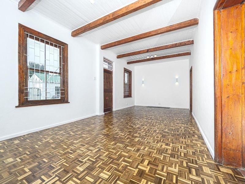 Spacious living area featuring classic parquet flooring, exposed timber ceiling beams, and characterful leaded glass windows with security bars.