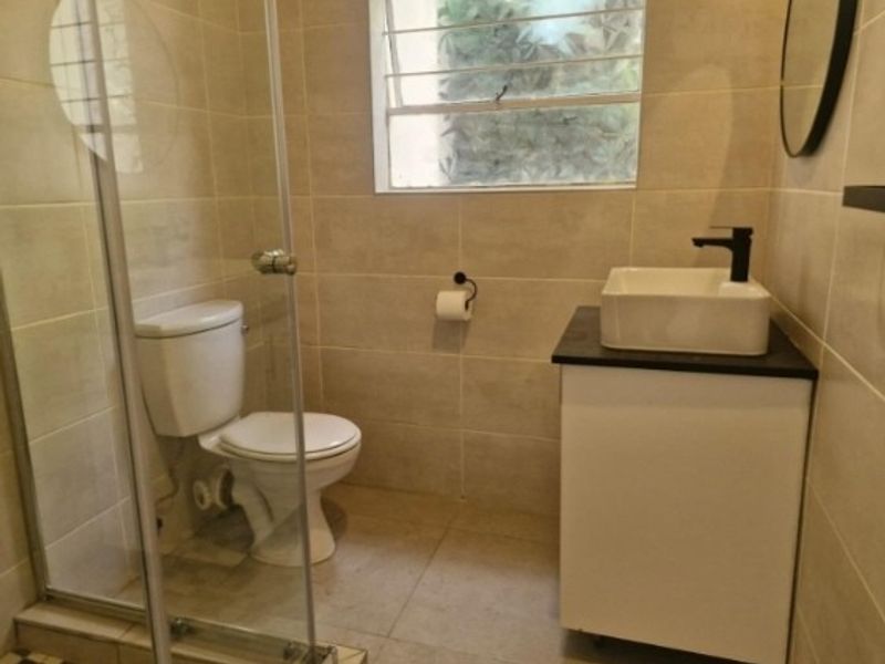 A clean, modern bathroom featuring a glass-enclosed shower, a vessel sink vanity, and neutral wall tiling.