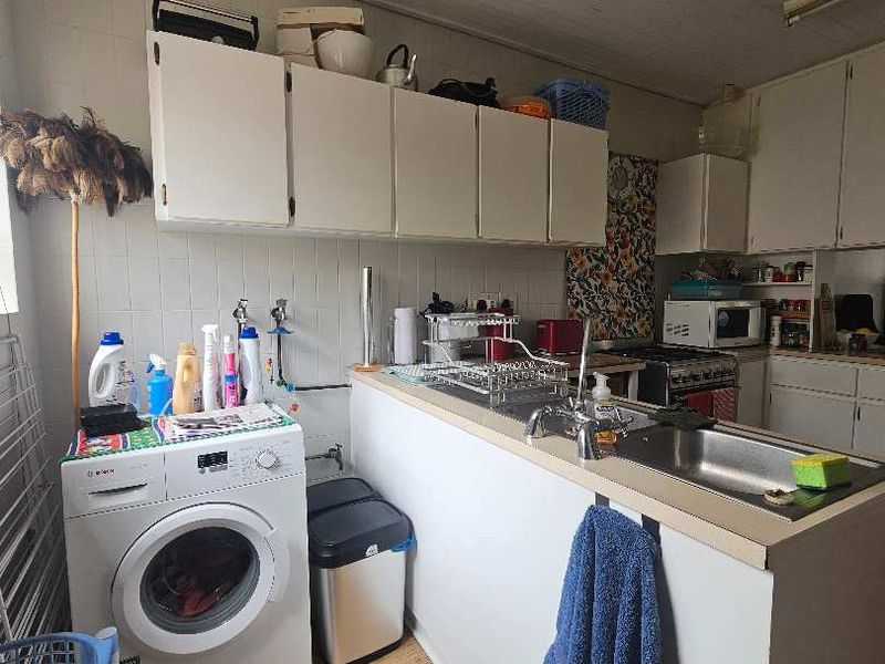 A functional kitchen featuring built-in cabinetry, a stainless steel sink, and tiled backsplash, offering a practical layout with integrated laundry plumbing.