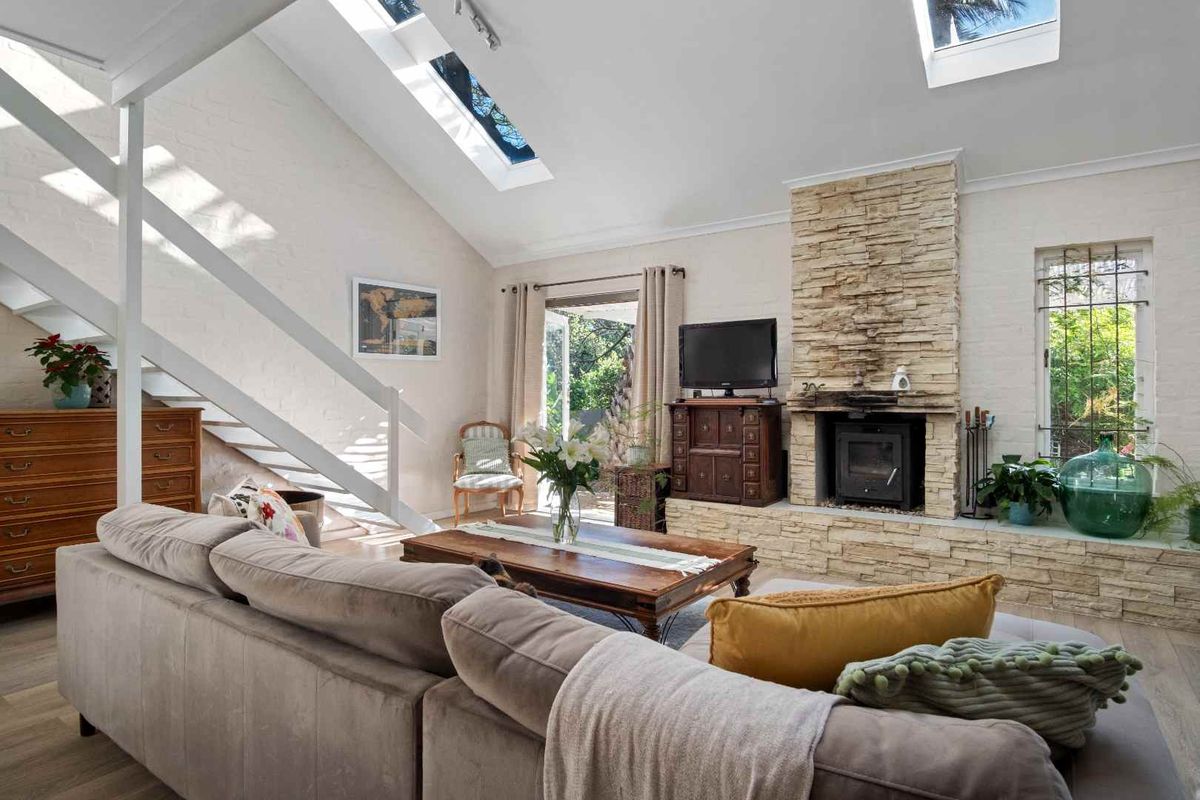 Spacious living room featuring a striking stone fireplace with a wood-burning stove, vaulted ceilings with skylights, and direct access to the outdoor area.