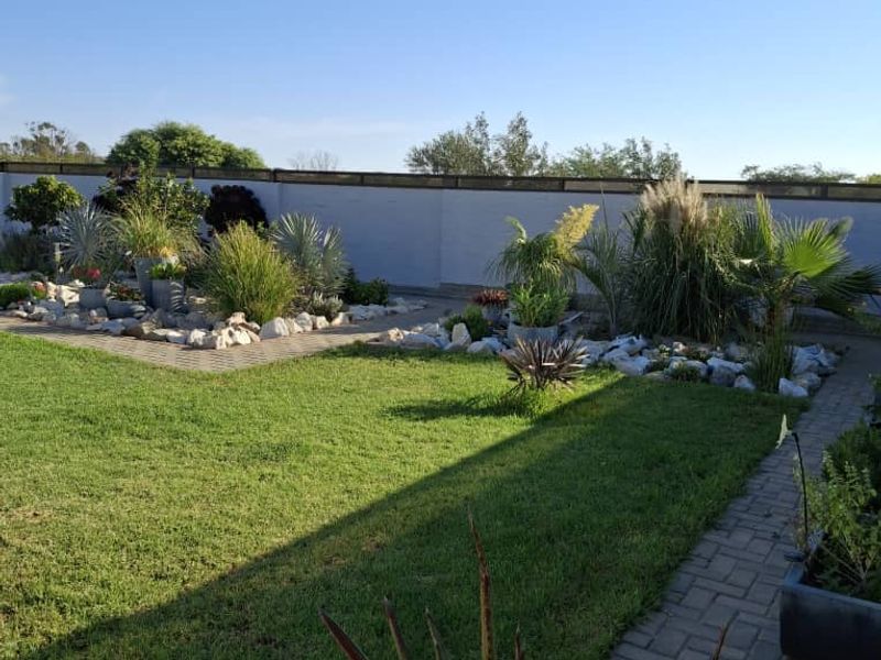 A well-maintained garden area featuring a manicured lawn, paved pathways, and established landscaped beds enclosed by a perimeter wall.