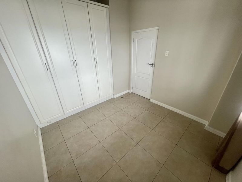 A clean, empty bedroom featuring neutral tiled flooring and white built-in cupboards, providing a versatile space ready for personalization.