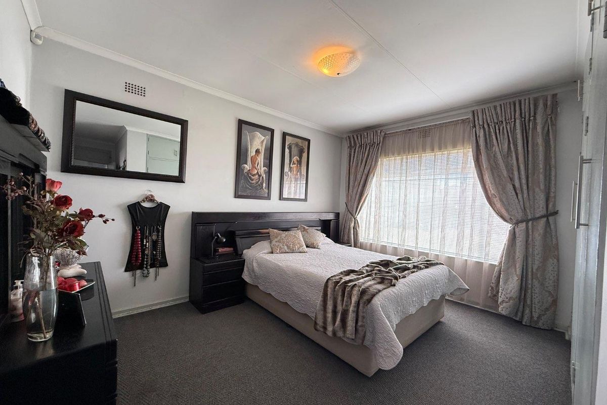 A well-maintained bedroom featuring neutral carpeting, a large window with curtain treatments, and a built-in headboard unit.