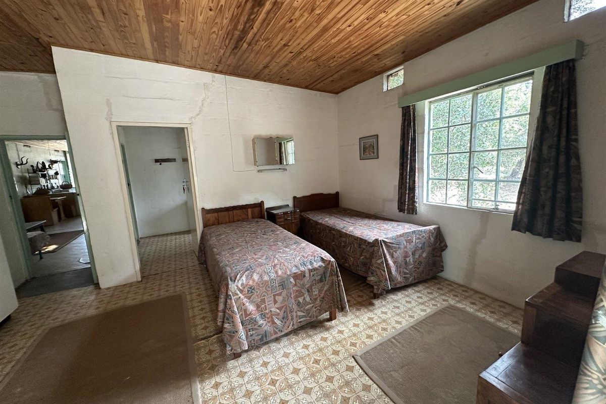 A rustic bedroom featuring a timber-clad ceiling, tiled flooring, and a large window, offering a dated aesthetic in need of modernization.
