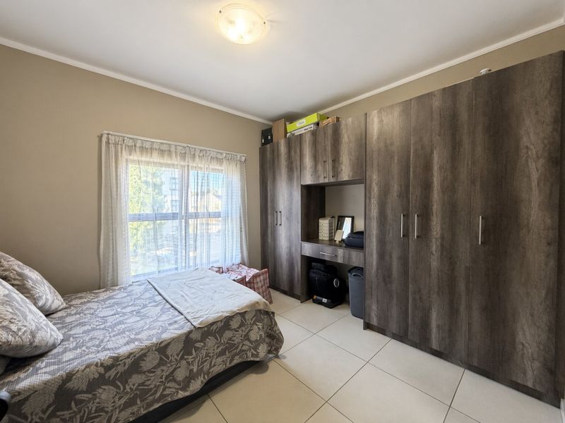 A well-maintained bedroom featuring large built-in cupboards with an integrated vanity and neutral tiled flooring.