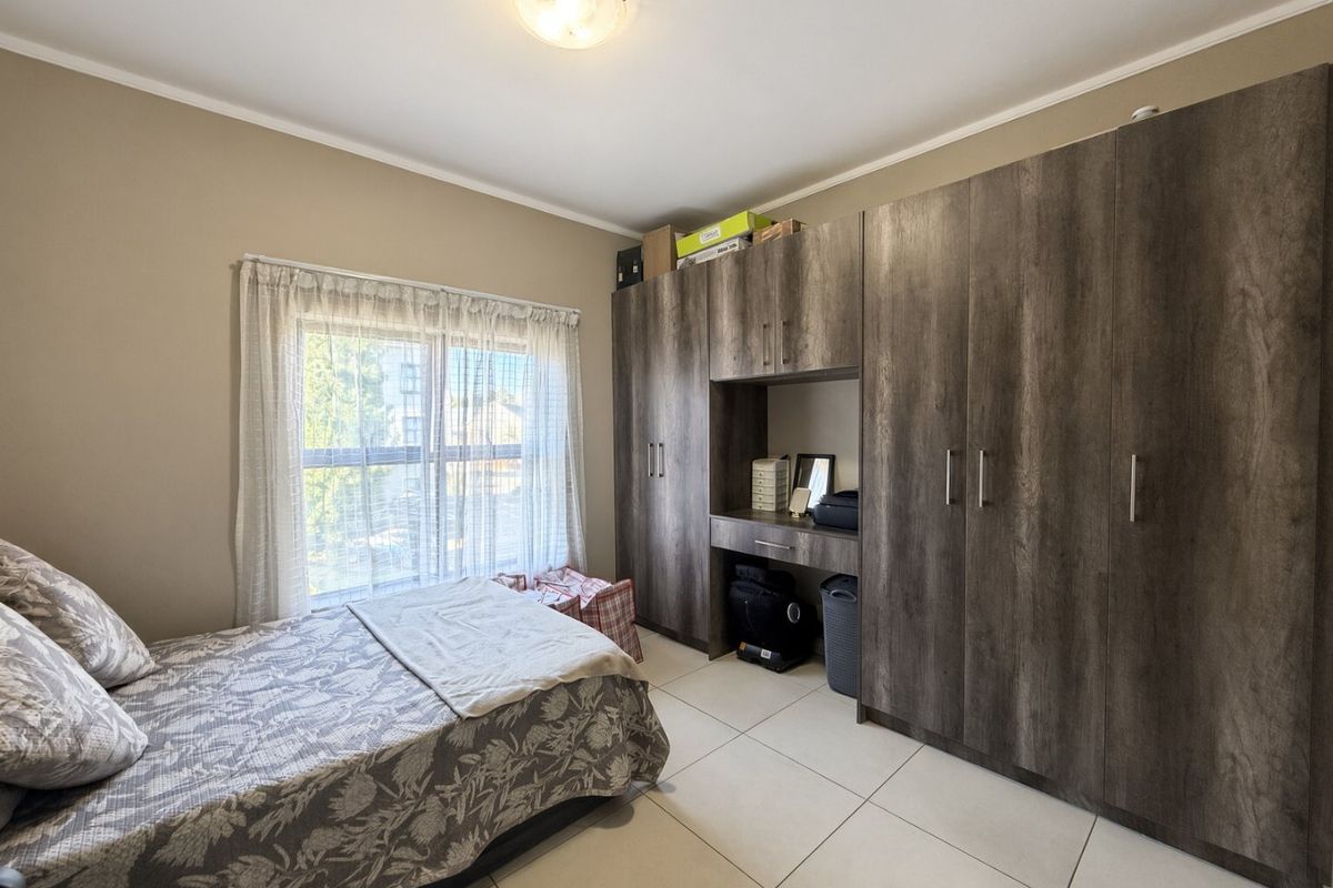 A well-maintained bedroom featuring large built-in cupboards with an integrated vanity and neutral tiled flooring.