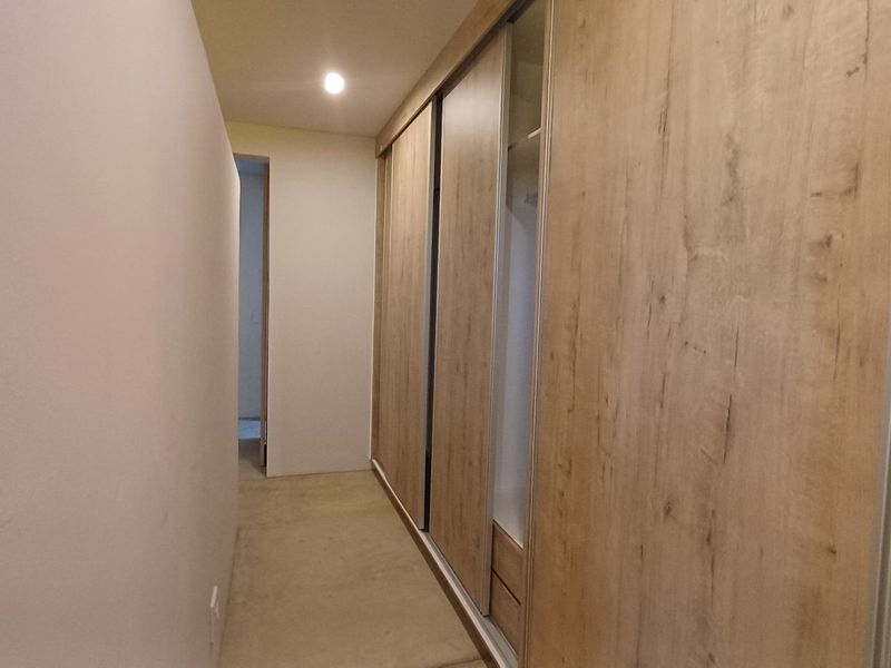 A clean hallway featuring modern wood-finish built-in sliding door wardrobes and recessed ceiling lighting.