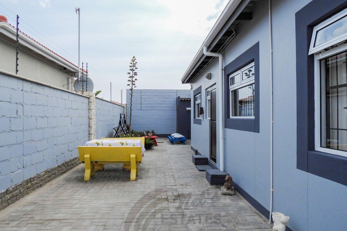 A paved rear courtyard area featuring a side entrance to the house, enclosed by perimeter boundary walls with security fencing.