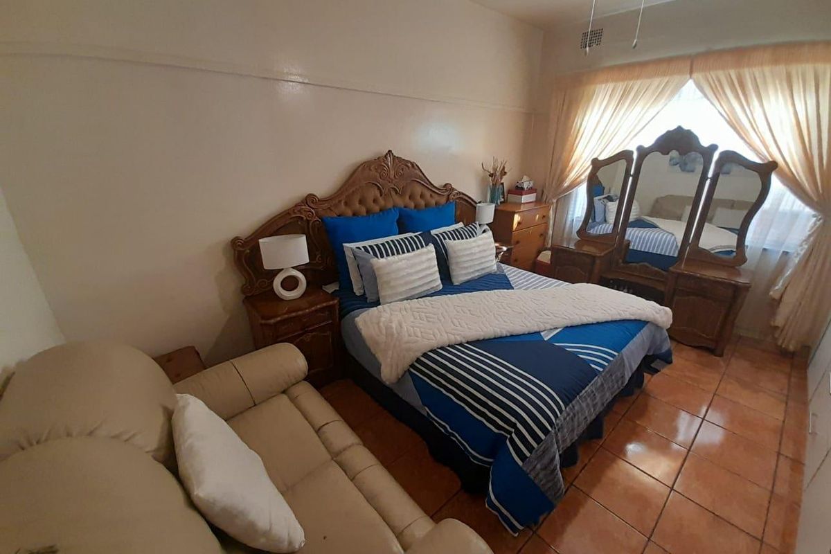 A bedroom featuring tiled flooring, a ceiling fan, and large windows with curtains, providing a functional living space.