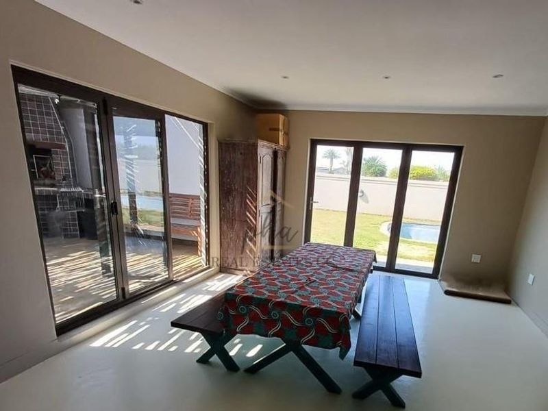 Open-plan living area featuring tiled floors, recessed lighting, and large aluminium sliding doors providing direct access to the garden and pool area.
