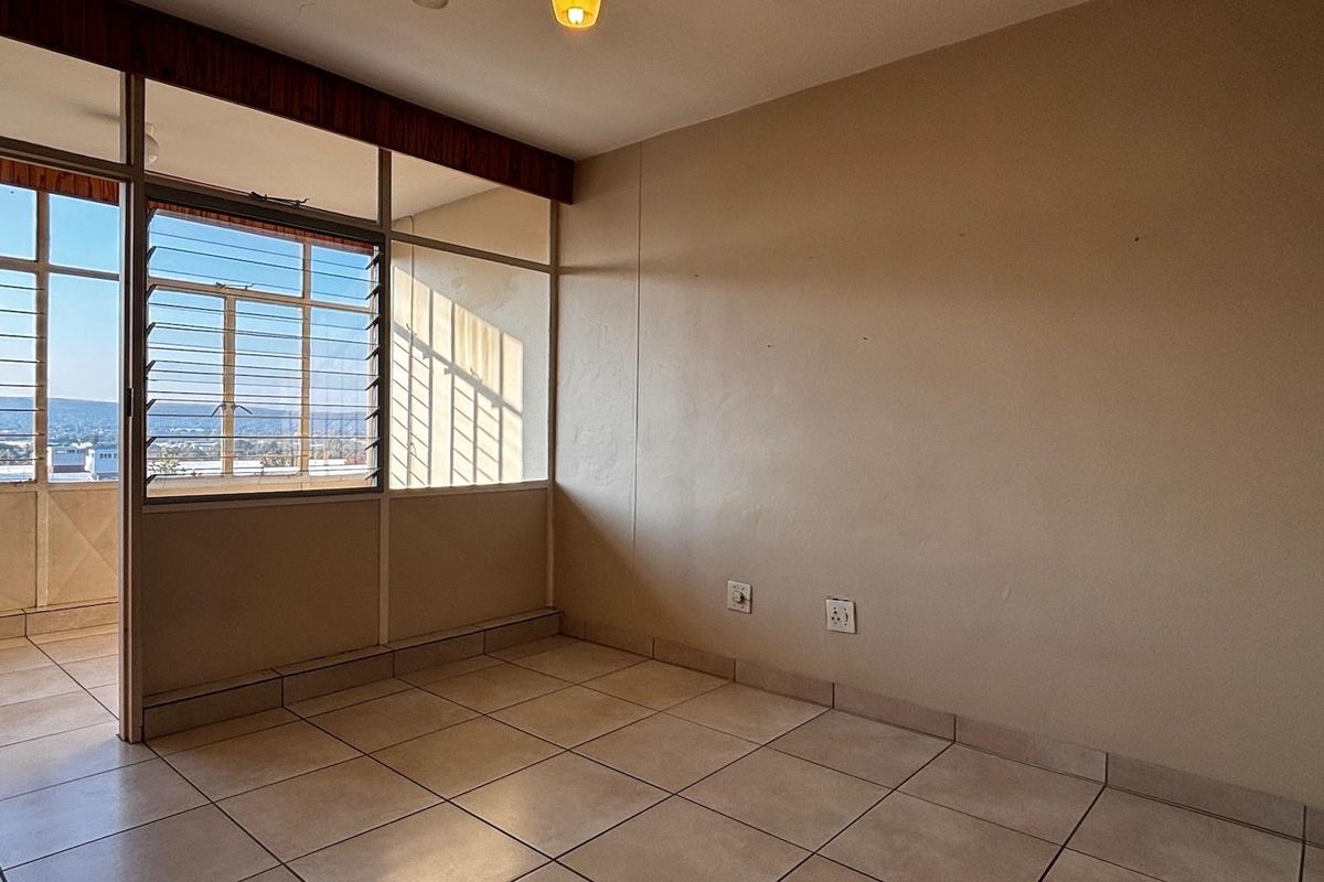 An empty bedroom featuring tiled flooring, large windows with security bars, and access to an adjacent balcony area.