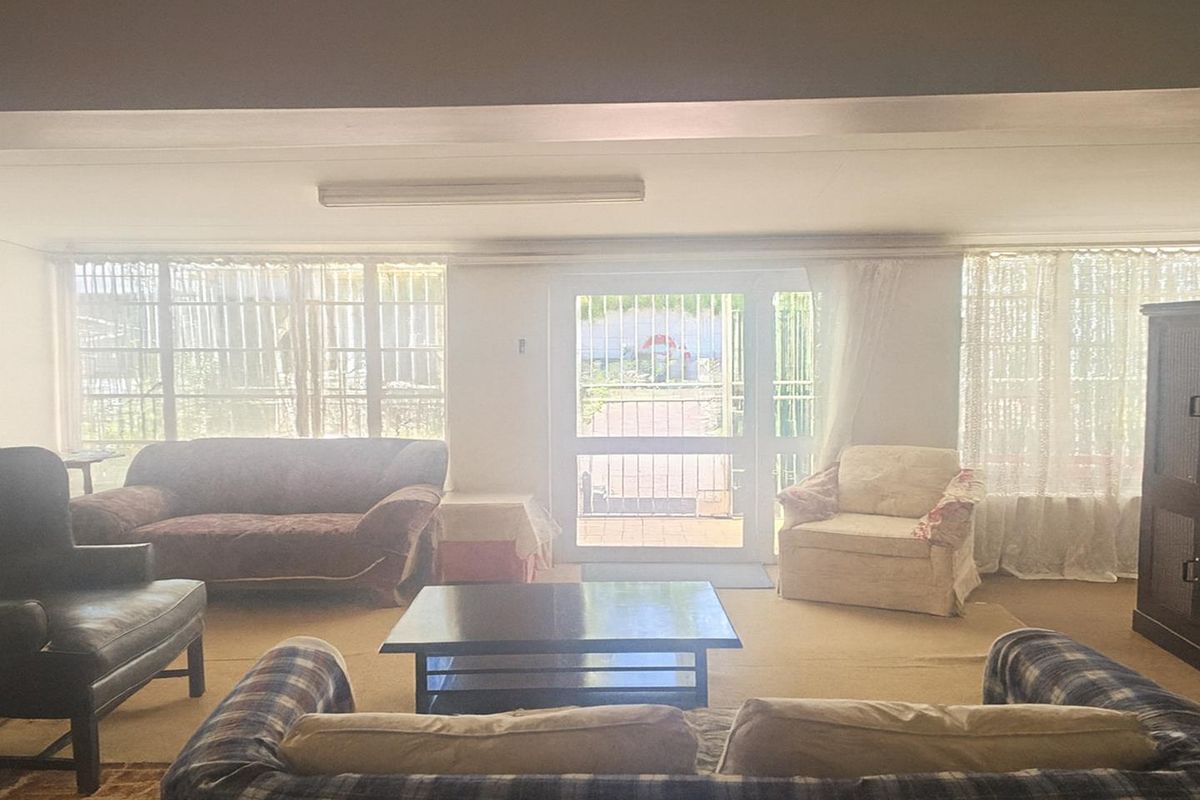 A spacious living room featuring large windows with security bars and a glass-panelled door providing direct access to the outdoor area.
